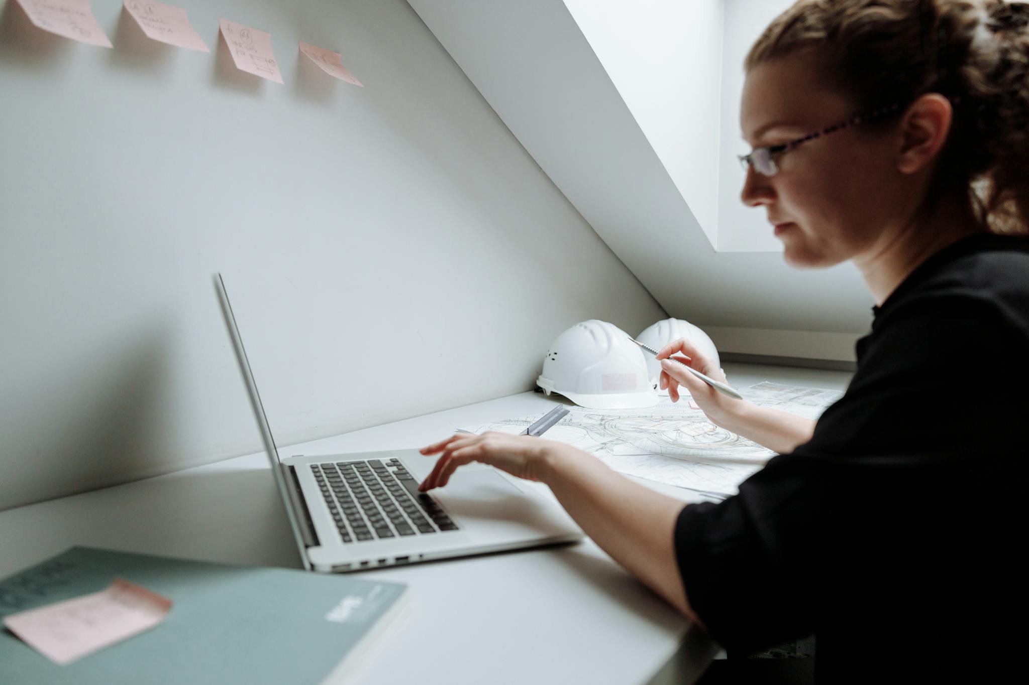 A focused architect working on building designs using a laptop in a modern office setting.